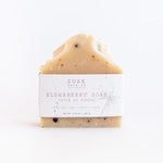 Load image into Gallery viewer, A bar of SOAK Elderberry Soap, placed on a white surface, with a label that includes the brand name and product details.