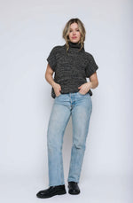 Load image into Gallery viewer, Woman wearing a black turtleneck sleeveless sweater and light blue jeans on a white background