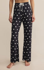 Load image into Gallery viewer, Person wearing black pajama pants with white ghost pattern on a beige background