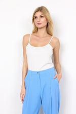 Load image into Gallery viewer, A woman wearing a white tank top with thin adjustable straps and a rounded neckline, paired with blue trousers.