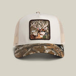 Load image into Gallery viewer, White and camouflage trucker hat with a deer patch on a beige background
