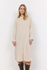 Load image into Gallery viewer, A woman standing against a white background wearing a beige long-sleeved buttoned dress that reaches her knees.
