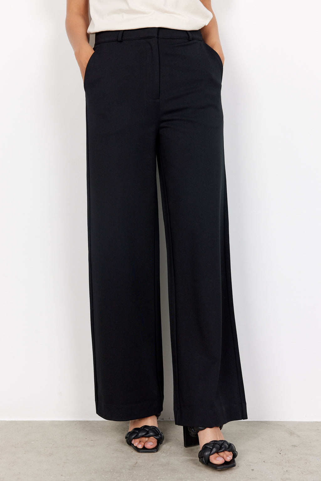 Person wearing black wide-leg pants against a white background. Pants feature pockets and elastic waistband. 
