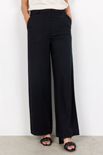 Load image into Gallery viewer, Person wearing black wide-leg pants against a white background. Pants feature pockets and elastic waistband. 
