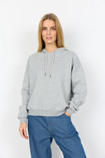 Load image into Gallery viewer, Woman wearing a gray light grey hoodie and blue pants on a white background
