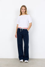 Load image into Gallery viewer, Woman wearing a white top and navy pants with drawstring waistband with pink stripe against a white background
