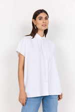 Load image into Gallery viewer, A woman wearing a white, short-sleeved, button-up shirt with a traditional collar, paired with blue jeans.
