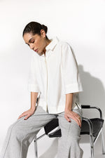 Load image into Gallery viewer, Woman sitting on a chair wearing a white shirt and gray pants against a white background
