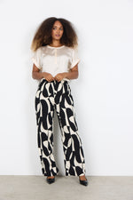 Load image into Gallery viewer, Woman wearing a white blouse and black and white patterned pants against a white background
