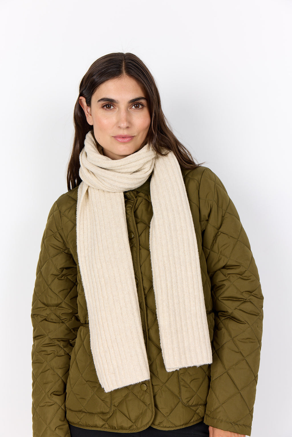 Woman wearing a green quilted jacket and a long cream scarf on a white background