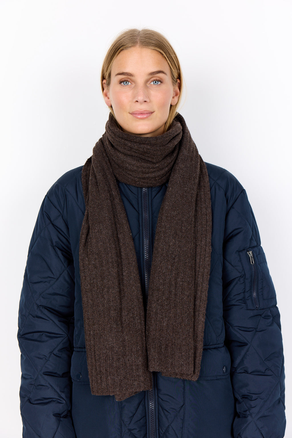 Woman wearing a dark blue coat and brown scarf on a white background