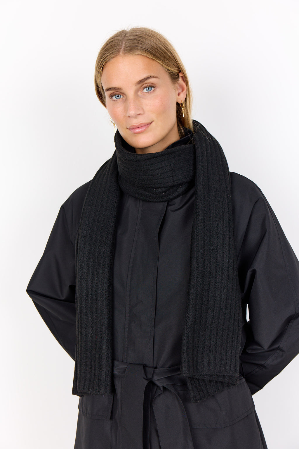 Woman wearing a black ribbed scarf and coat against a white background