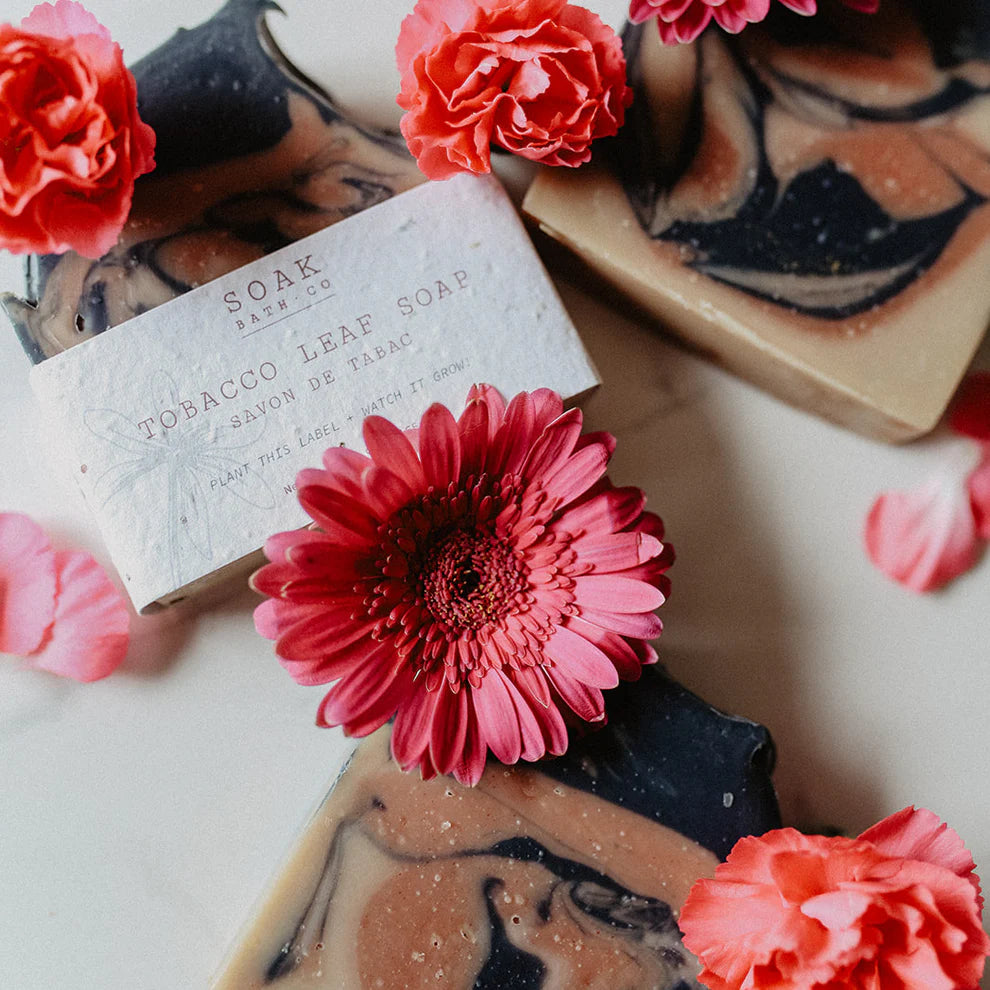Bar of soap with 'SOAK' branding surrounded by pink flowers on a light background