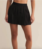 Load image into Gallery viewer, Black  pleated skirt worn by a person on a beige background
