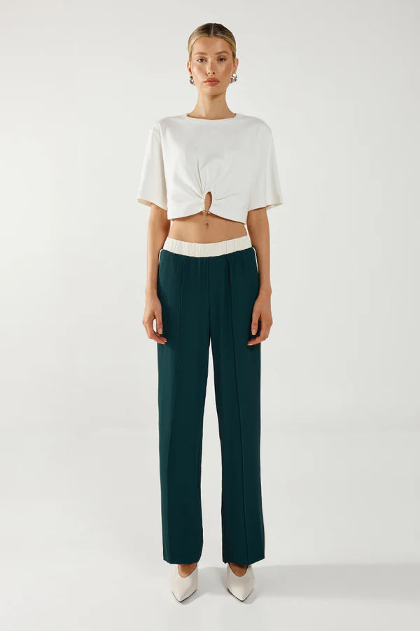 Woman wearing a white top and dark green pants on a white background