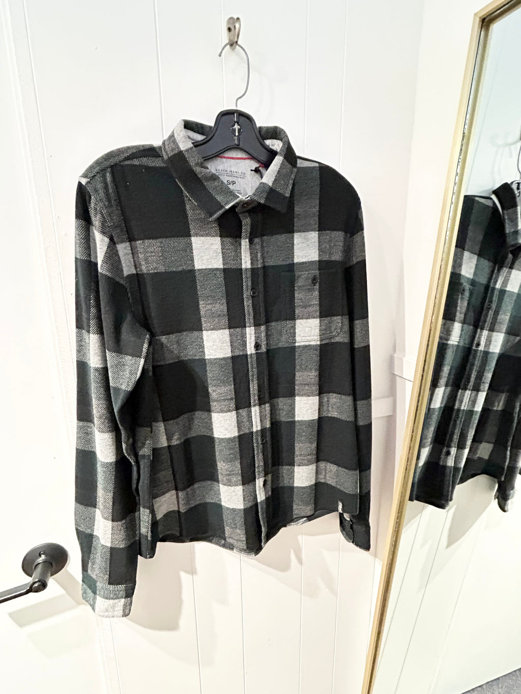 Olive and grey checkered shirt on a hanger with a mirror reflection.