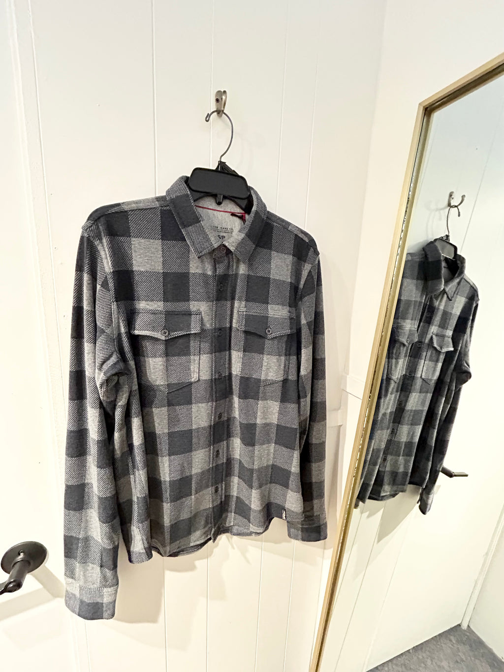 Gray and navy plaid shirt on a hanger in front of a mirror.