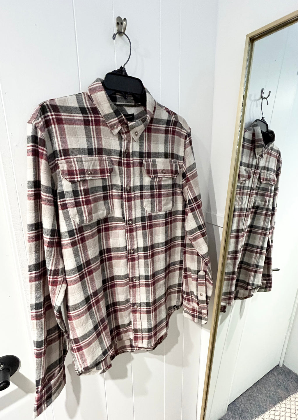 Plaid shirt on a hanger with a full-length mirror reflection.