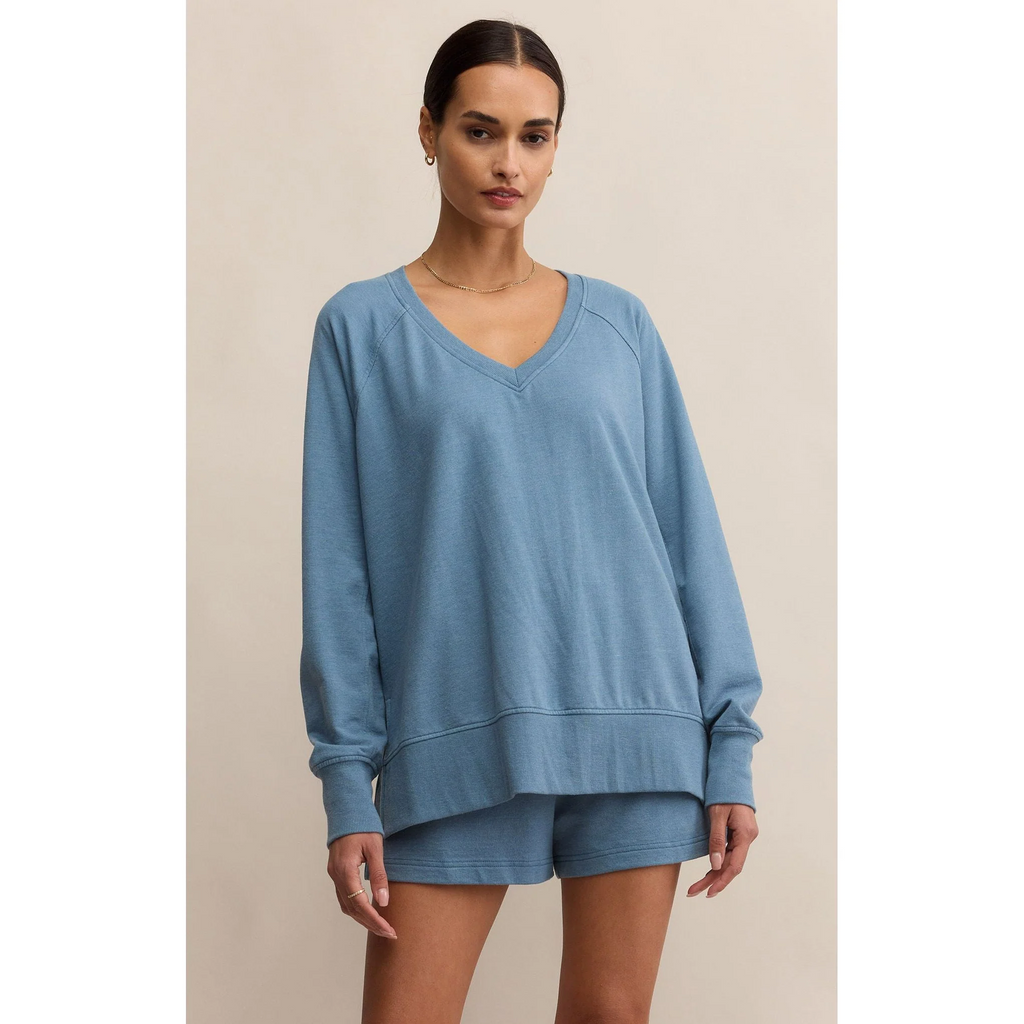 Woman wearing a blue lounge set on a beige background. Top has rib cuffs and waistband. V-neck neckline. Oversized/relaxed fit.