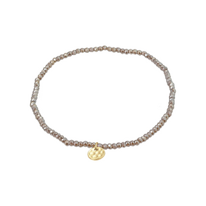 Delicate grey beaded bracelet with a gold charm on a white background