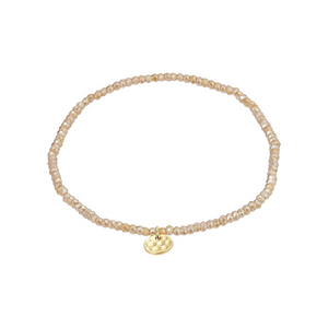 Beaded nude peach bracelet with a gold charm on a white background