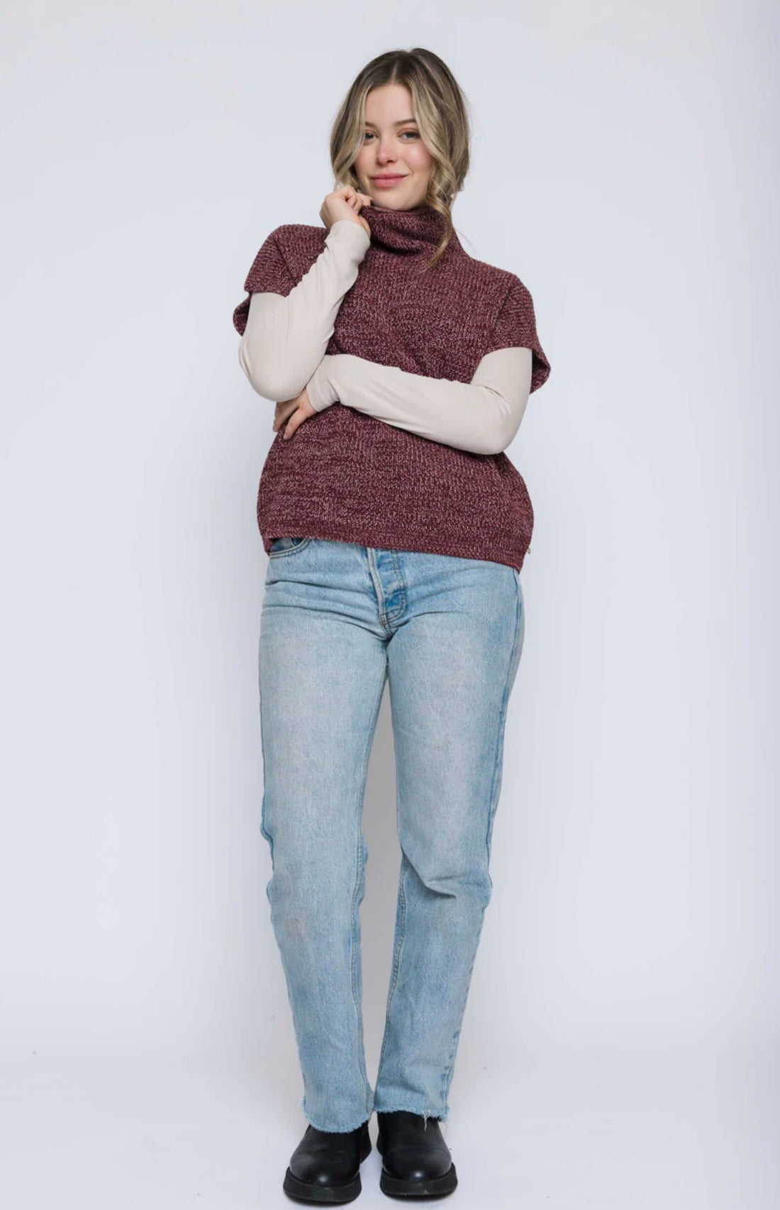 Woman wearing a wine coloured turtleneck sweater and light blue jeans on a white background