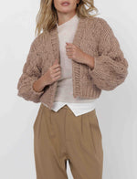 Load image into Gallery viewer, Woman wearing a beige knitted cardigan over a white shirt and beige pants on a white background
