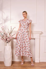 Load image into Gallery viewer, Woman in a floral midi dress standing in a room with a vase of flowers and a fireplace.
