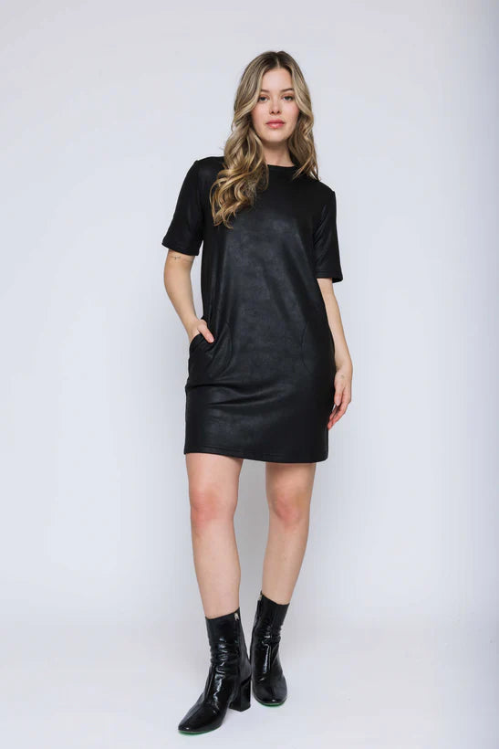 Woman wearing a black faux leather shift dress with black boots on a white background
