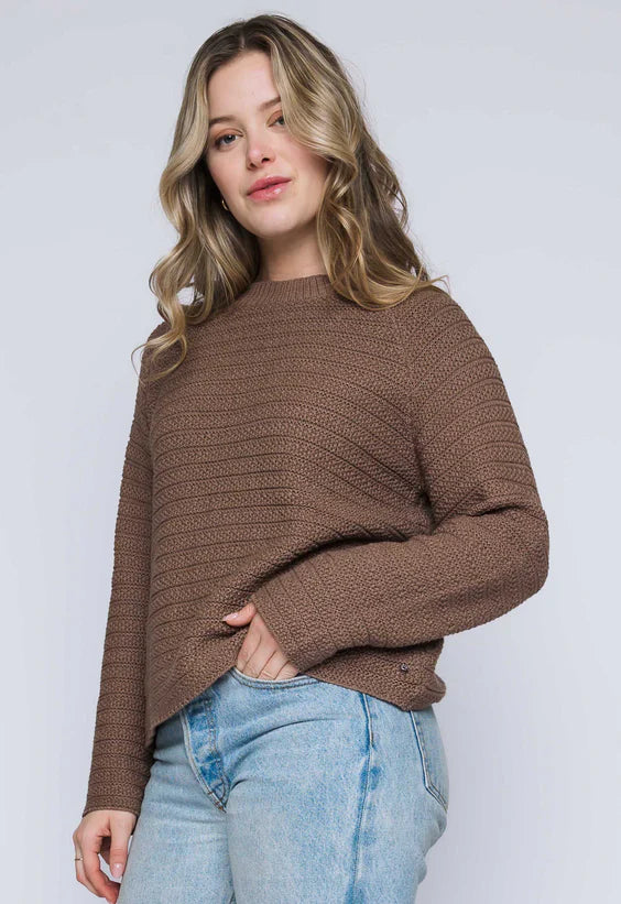 Woman wearing a brown textured  sweater and light blue jeans against a white background
