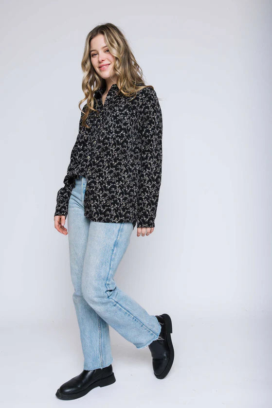 Woman wearing a black patterned shirt, light blue jeans, and black shoes on a white background