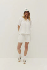 Load image into Gallery viewer, Person wearing a white linen shorts outfit with a cap on a plain background
