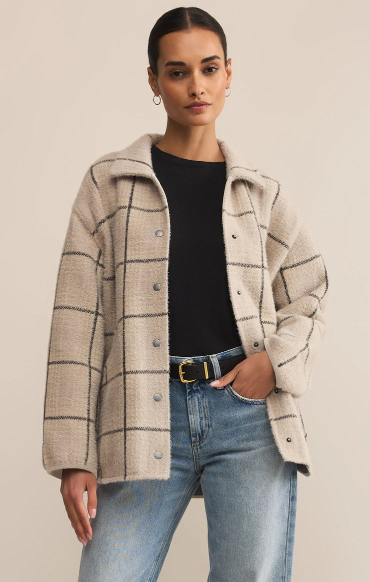 Woman wearing a plaid coat over a black shirt and blue jeans on a beige background