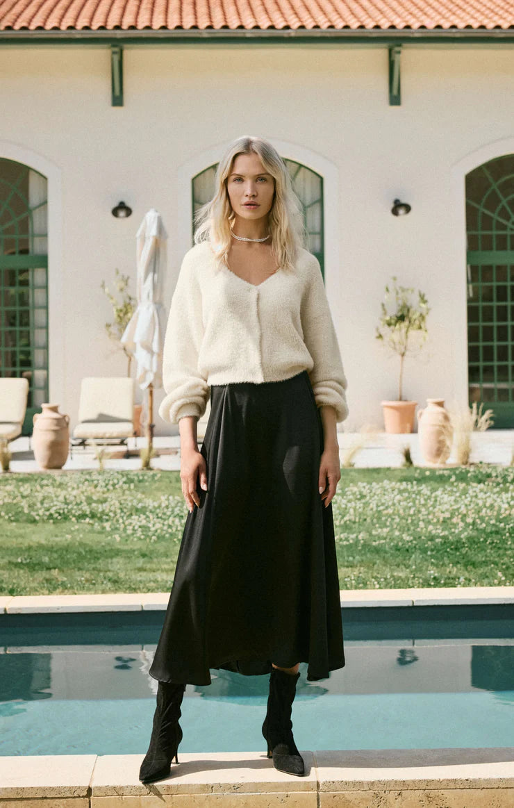 Woman in a white sweater and black A-line midi skirt standing by a pool with a building in the background