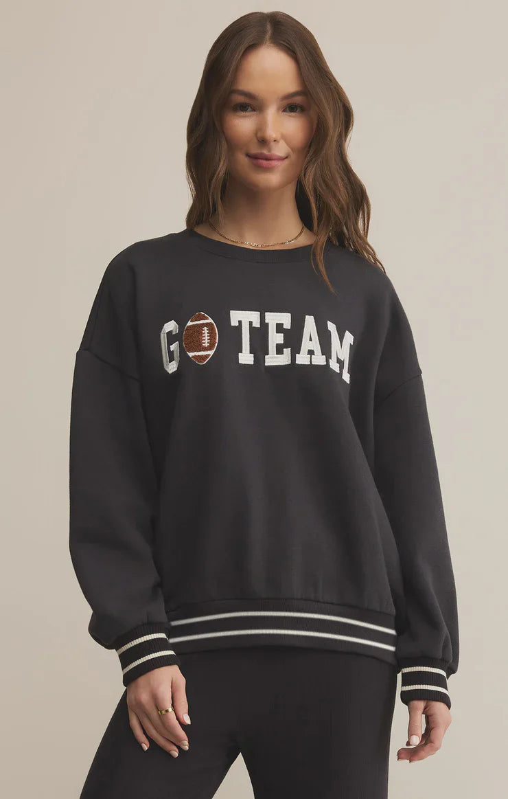 Woman wearing a black sweatshirt with 'GO TEAM' text and a football graphic on a beige background