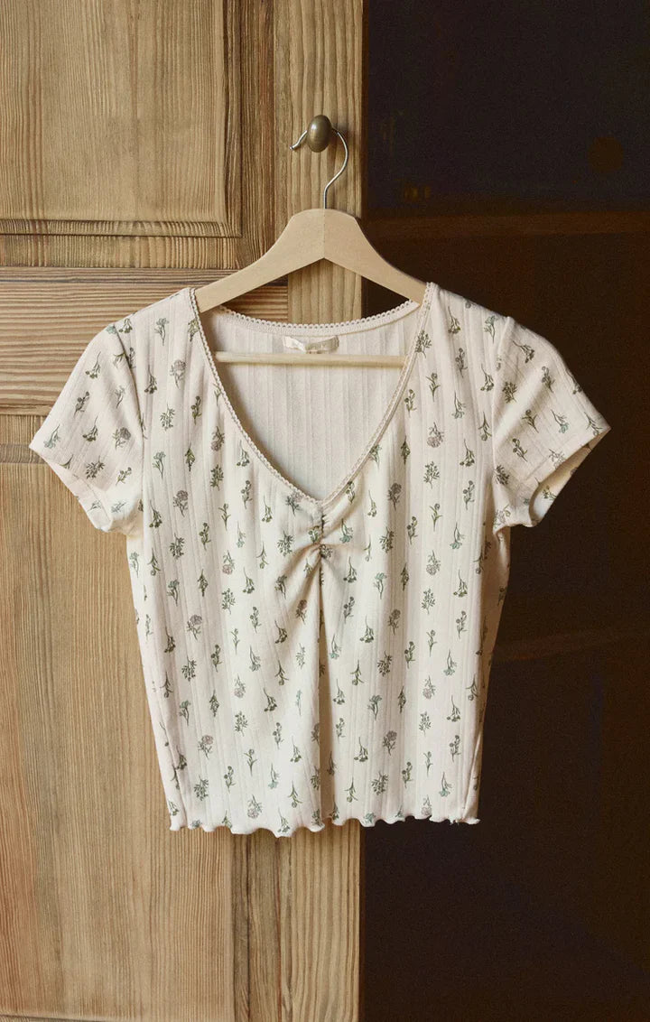 Beige floral  patterned top on a wooden hanger against a wooden door.