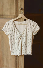 Load image into Gallery viewer, Beige floral  patterned top on a wooden hanger against a wooden door.
