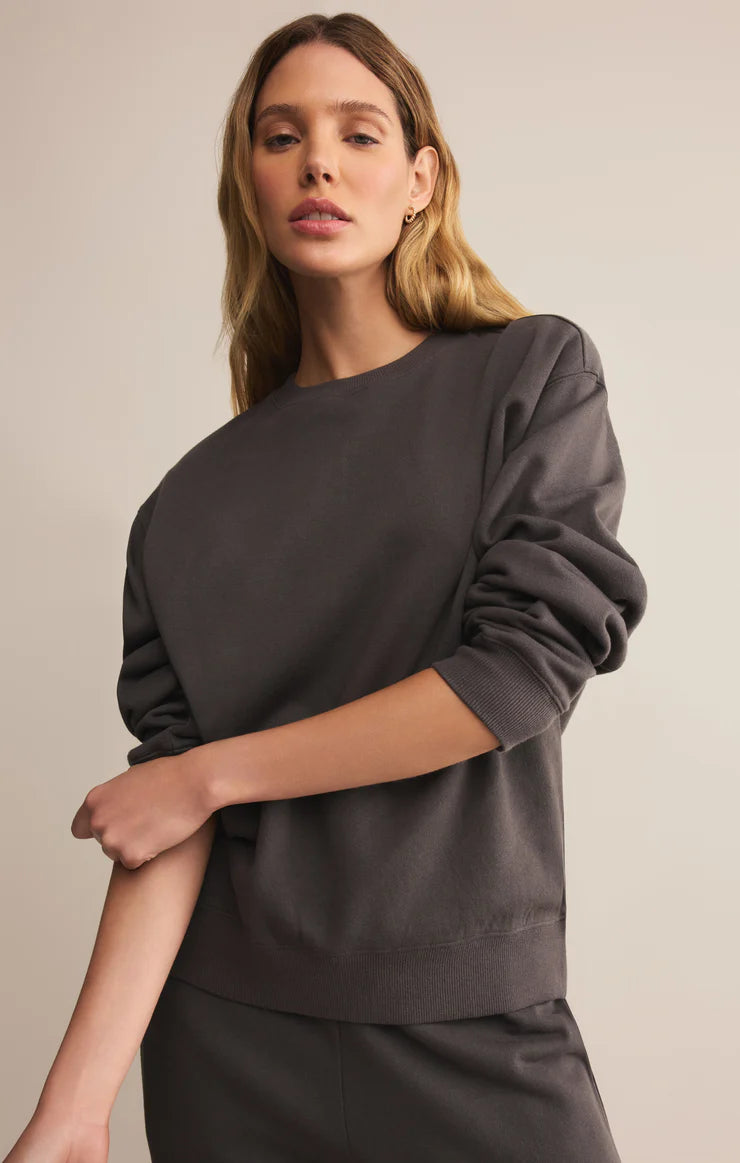 Woman wearing a washed black crewneck sweatshirt against a beige background