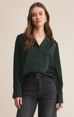 Load image into Gallery viewer, Woman wearing a green satin blouse and black pants against a beige background
