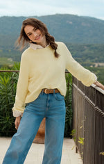 Load image into Gallery viewer, Woman wearing a yellow sweater and blue jeans standing outdoors with mountains in the background
