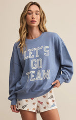Load image into Gallery viewer, Woman wearing a blue sweatshirt with 'LET'S GO TEAM' text and patterned shorts on a beige background
