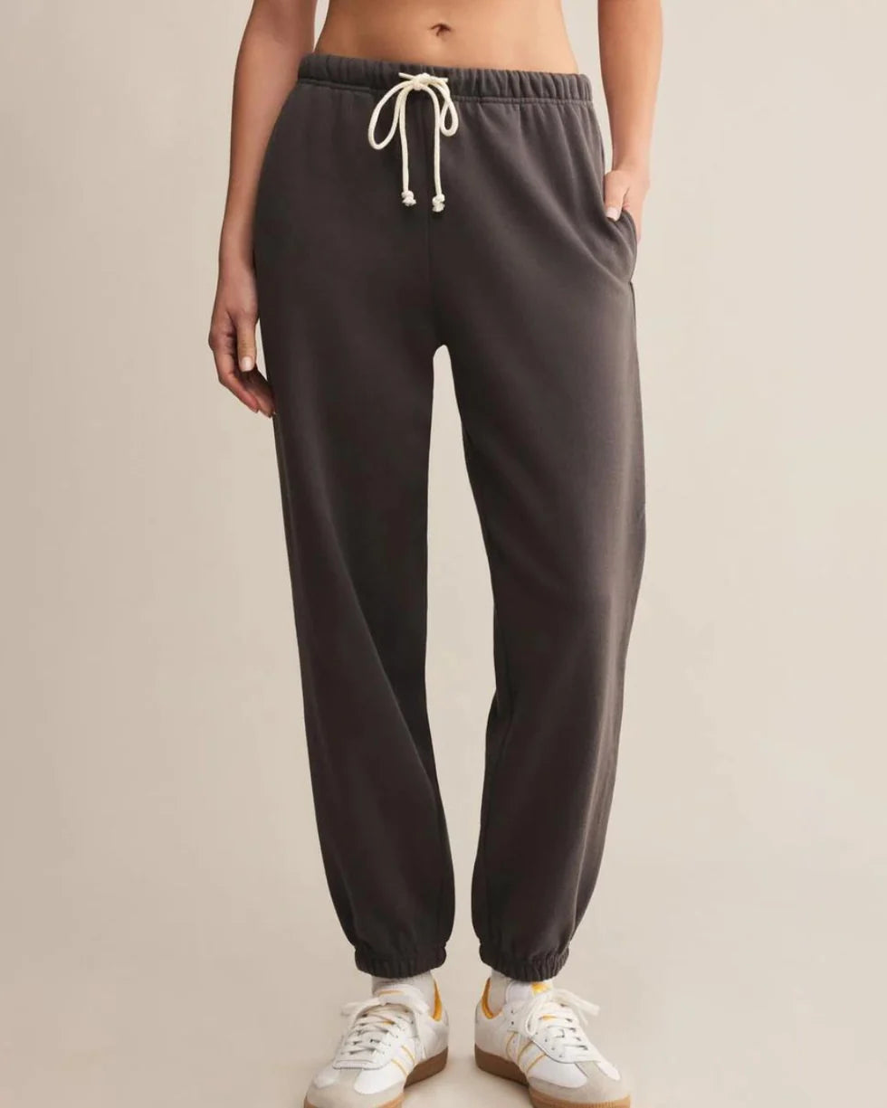 Washed black sweatpants worn by a person on a beige background