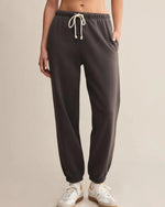 Load image into Gallery viewer, Washed black sweatpants worn by a person on a beige background
