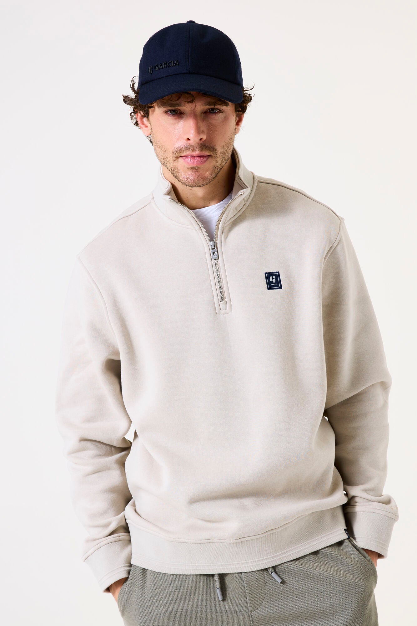 Man wearing a beige half-zip sweatshirt with a small logo on a white background