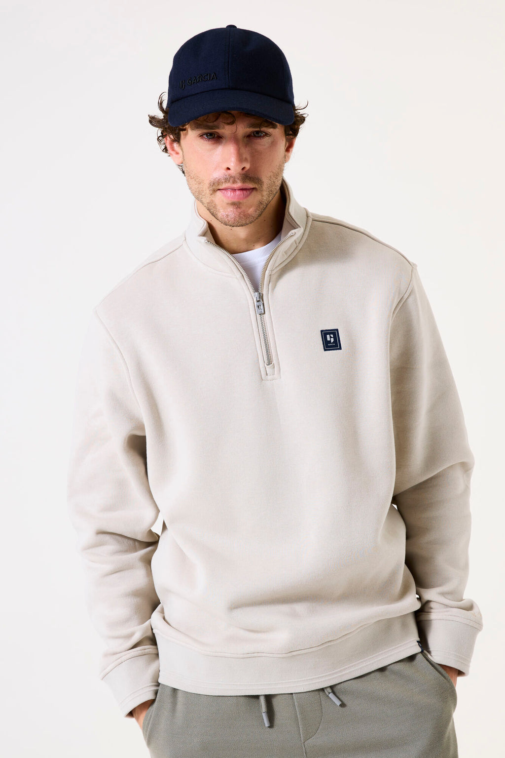 Man wearing a beige half-zip sweatshirt with a small logo on a white background