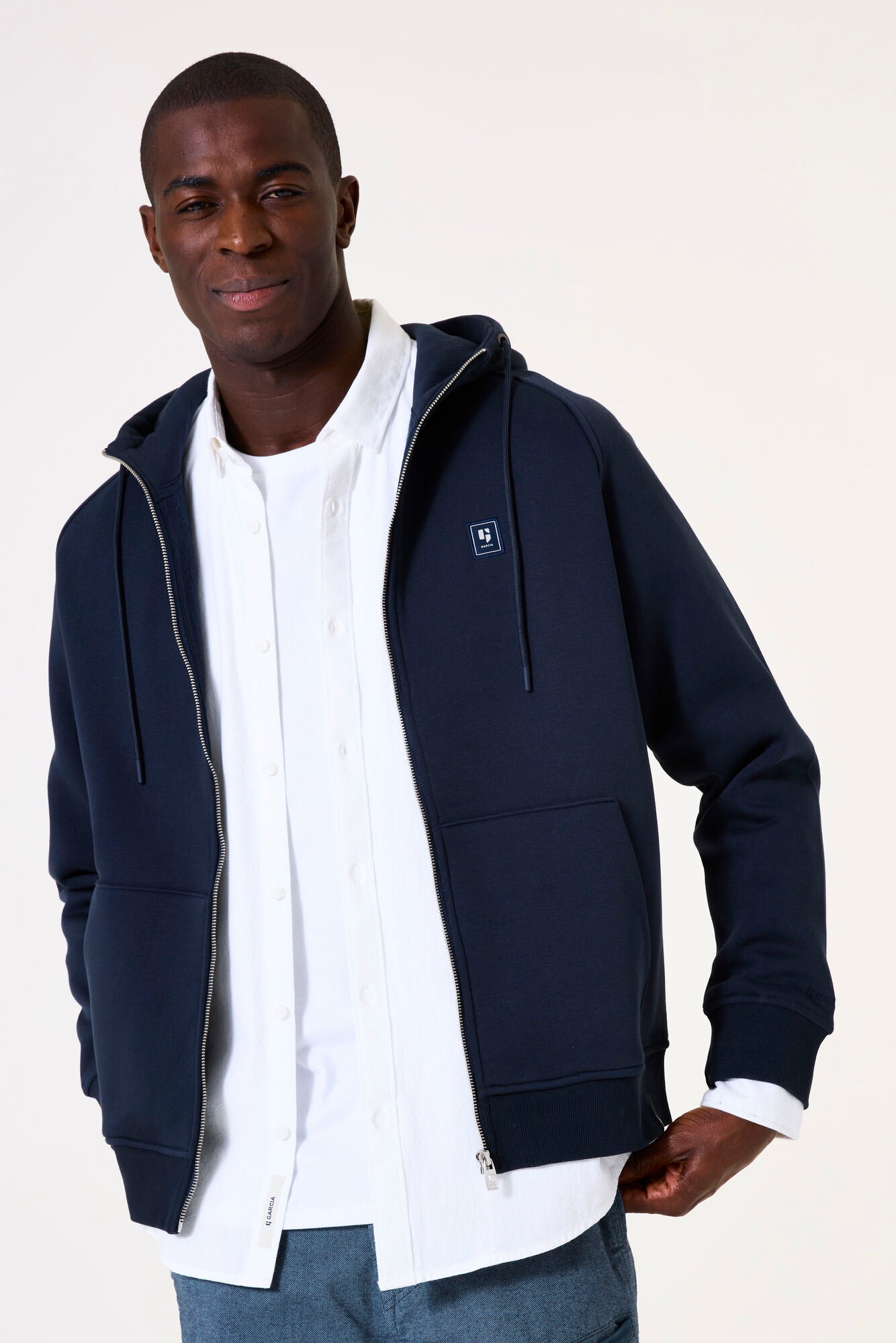 Man wearing a navy blue zip up hoodie over a white shirt on a white background