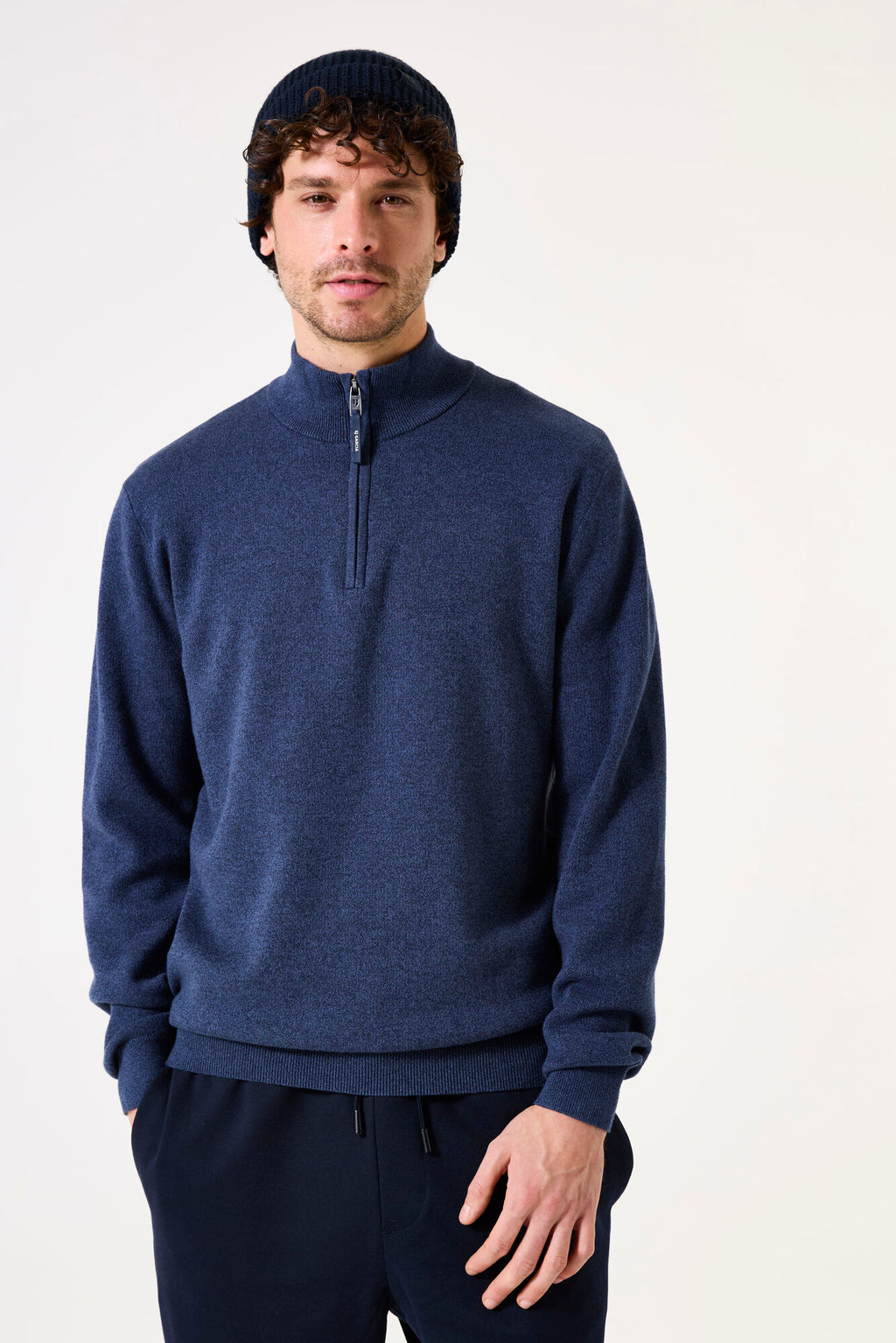 Man wearing a blue 1/4 zip pullover sweater and black beanie against a white background