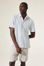 Load image into Gallery viewer, Man wearing a white striped short sleeved shirt and beige shorts against a plain background
