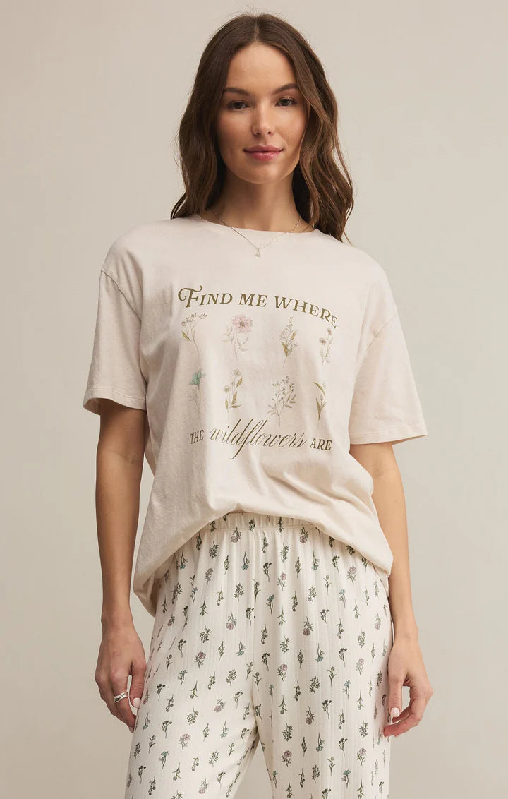 Woman wearing a beige t-shirt with text and floral design, standing against a plain background