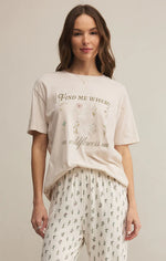 Load image into Gallery viewer, Woman wearing a beige t-shirt with text and floral design, standing against a plain background
